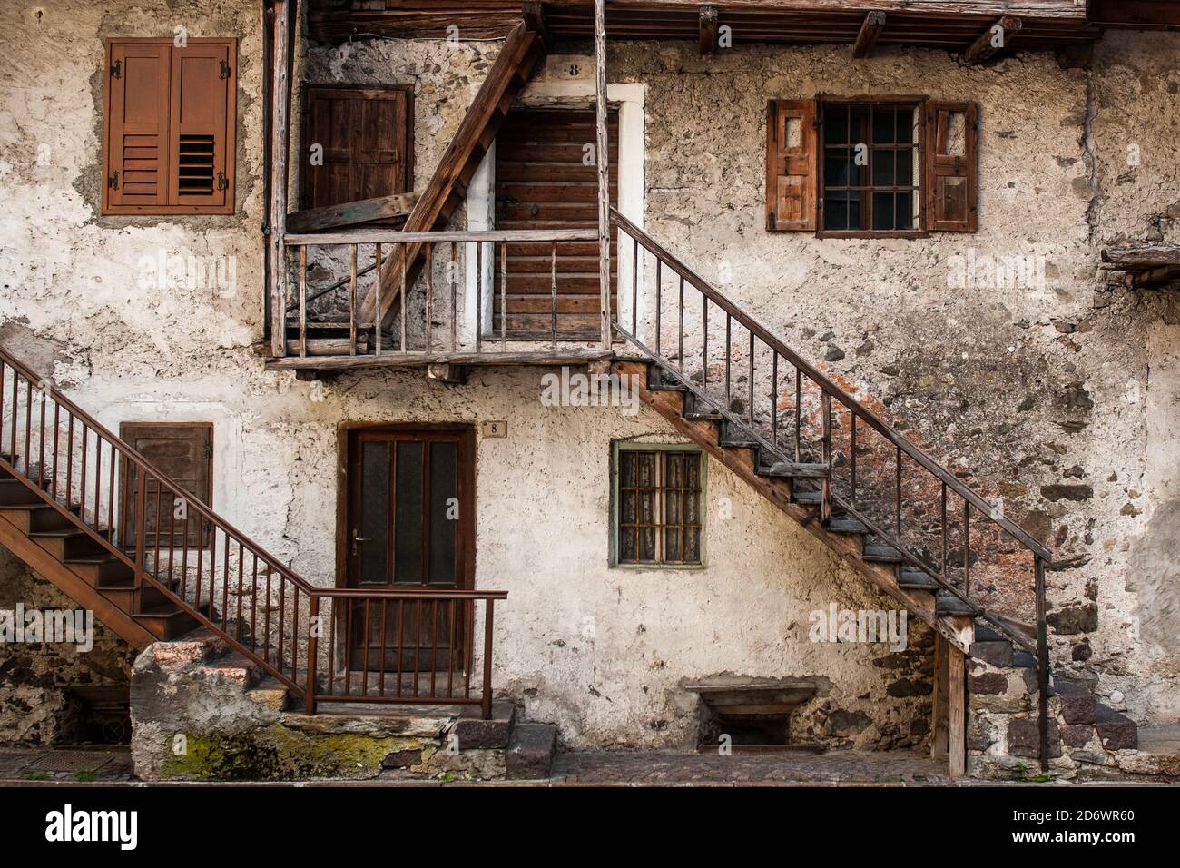 Una vecchia casa nel villaggio italiano di Mezzano, in Trentino Alto Adige con pareti bianche e finestre in legno marrone, porte e ringhiere Foto Stock