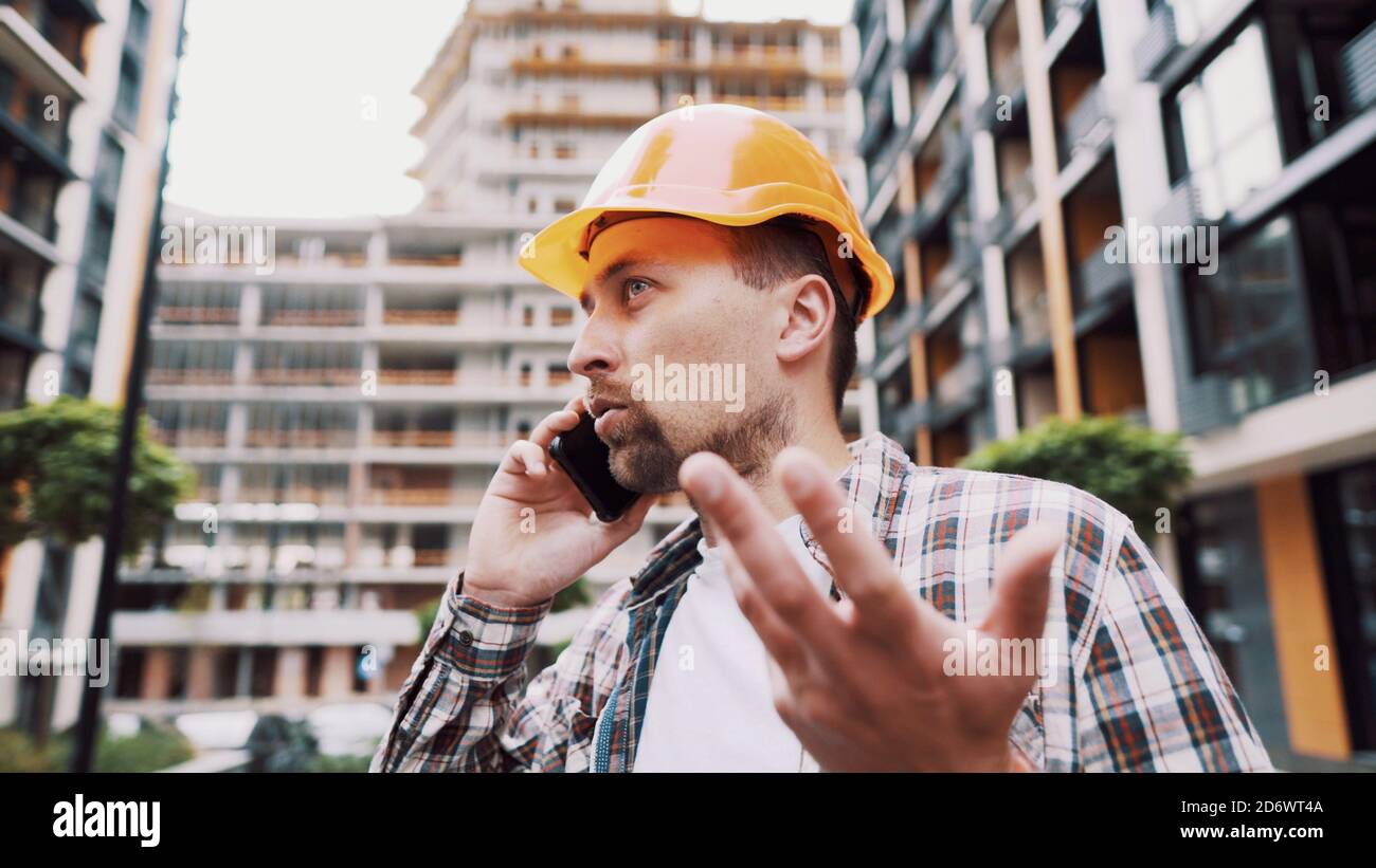 Tecnico che parla al telefono. Architetto utilizzando il telefono sul cantiere. Processo di controllo delle chiamate telefoniche dei caposquadra. Comunicazioni dei lavoratori edili in Foto Stock