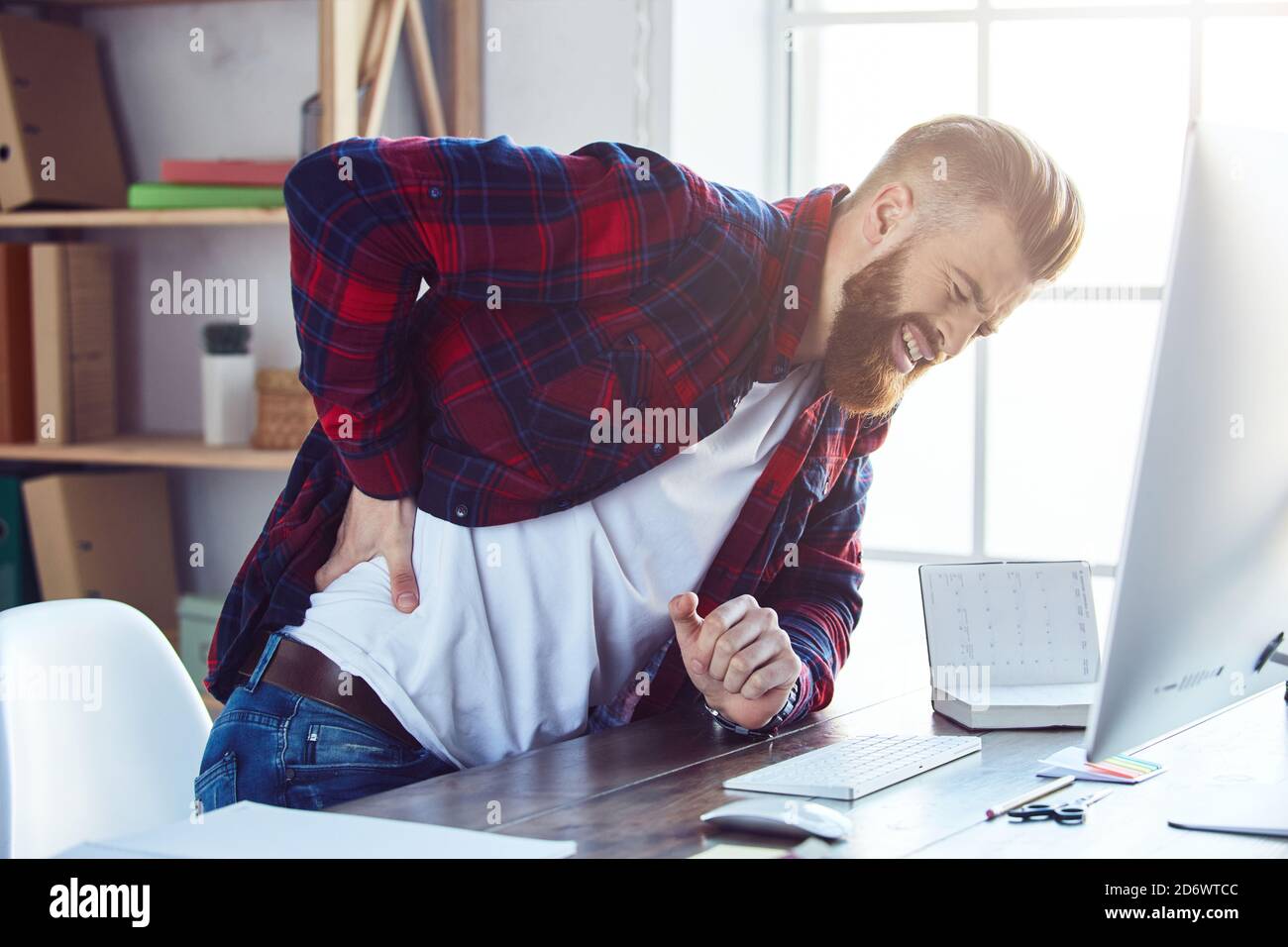Ragazzo sopportato che soffre di disagio mentre ha dolore alla schiena in studio creativo. Concetto di overworking Foto Stock