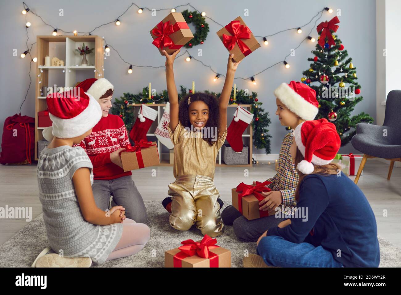 Gruppo di felici bambini multietnici che scambiano regali seduti a terra in soggiorno Foto Stock
