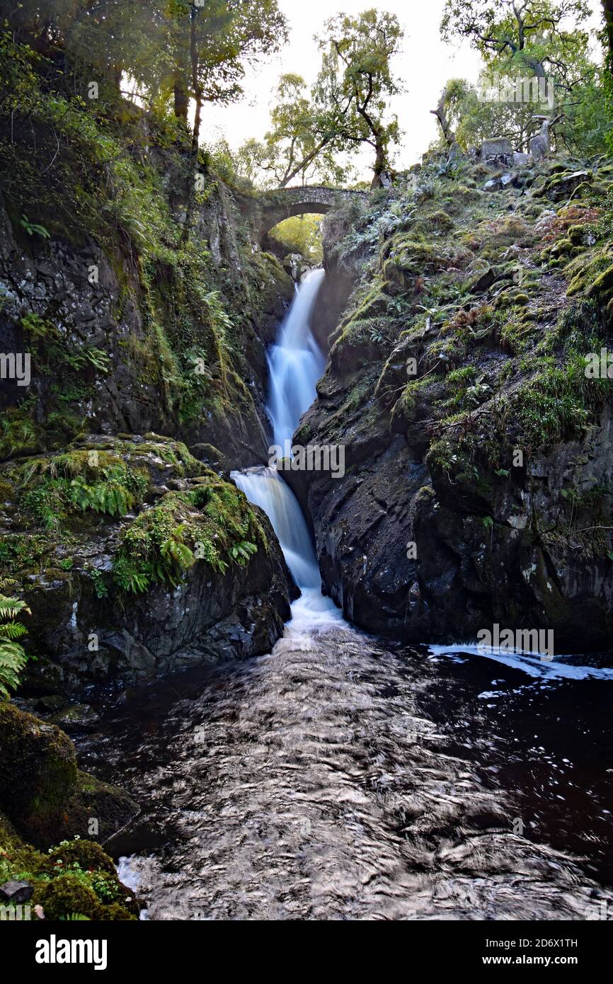 Aira Force Waterfall vicino Ullswater nel Lake District National Park, Inghilterra. Il sole sta iniziando a impostare con un bagliore giallo. Un ponte sulle cascate. Foto Stock