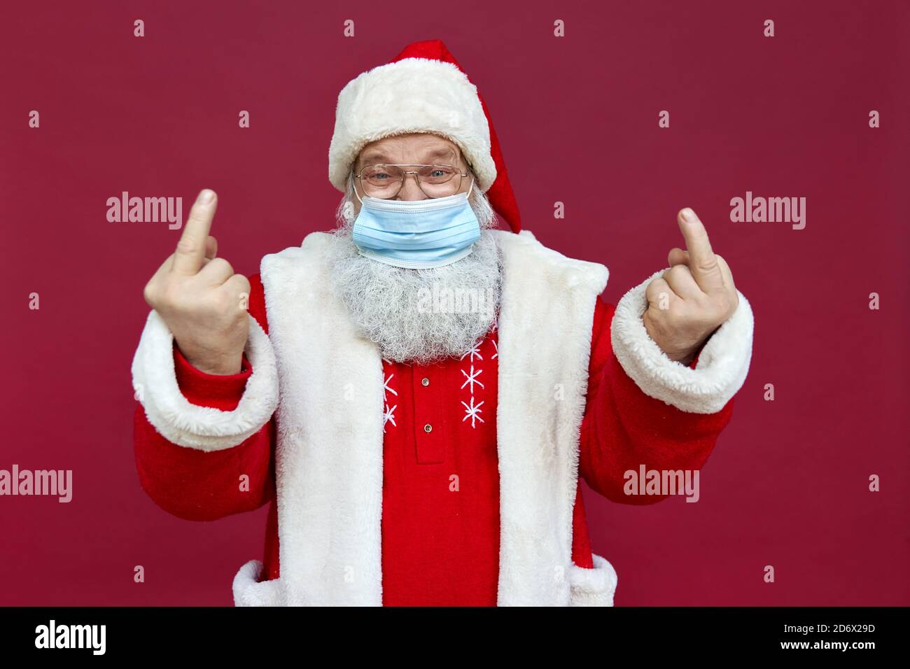 Babbo Natale indossa una maschera che mostra le dita centrali su sfondo rosso. Foto Stock