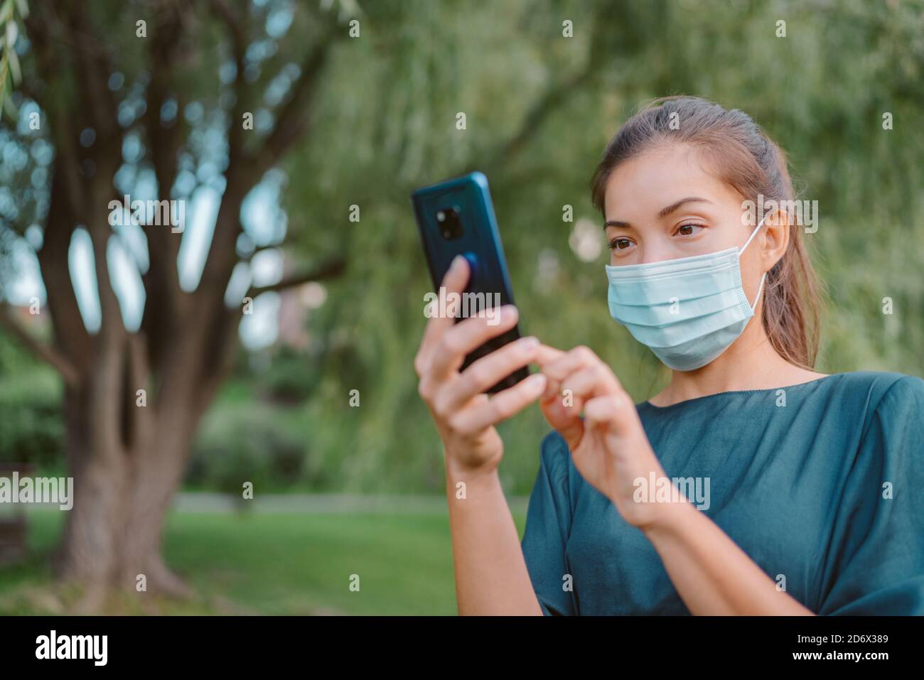Donna che indossa la maschera facciale utilizzando il telefono cellulare per l'applicazione di tracciamento del contatto mentre si cammina all'esterno durante la pandemia del coronavirus. Stile di vita della città delle persone Foto Stock