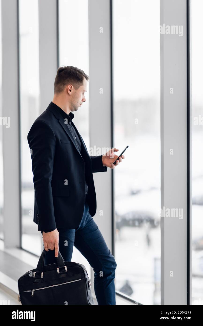 Uomo d'affari tramite telefono mobile app in aeroporto. Giovane professionista business man texting a piedi dello smartphone all'interno di edificio per uffici o terminale di un aeroporto Foto Stock