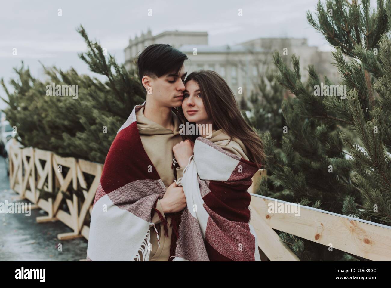 Primo piano esterno ritratto di giovane bella coppia sorridente felice impacchettato in coperta di tartan. Natale, Capodanno, vacanze invernali. Foto Stock