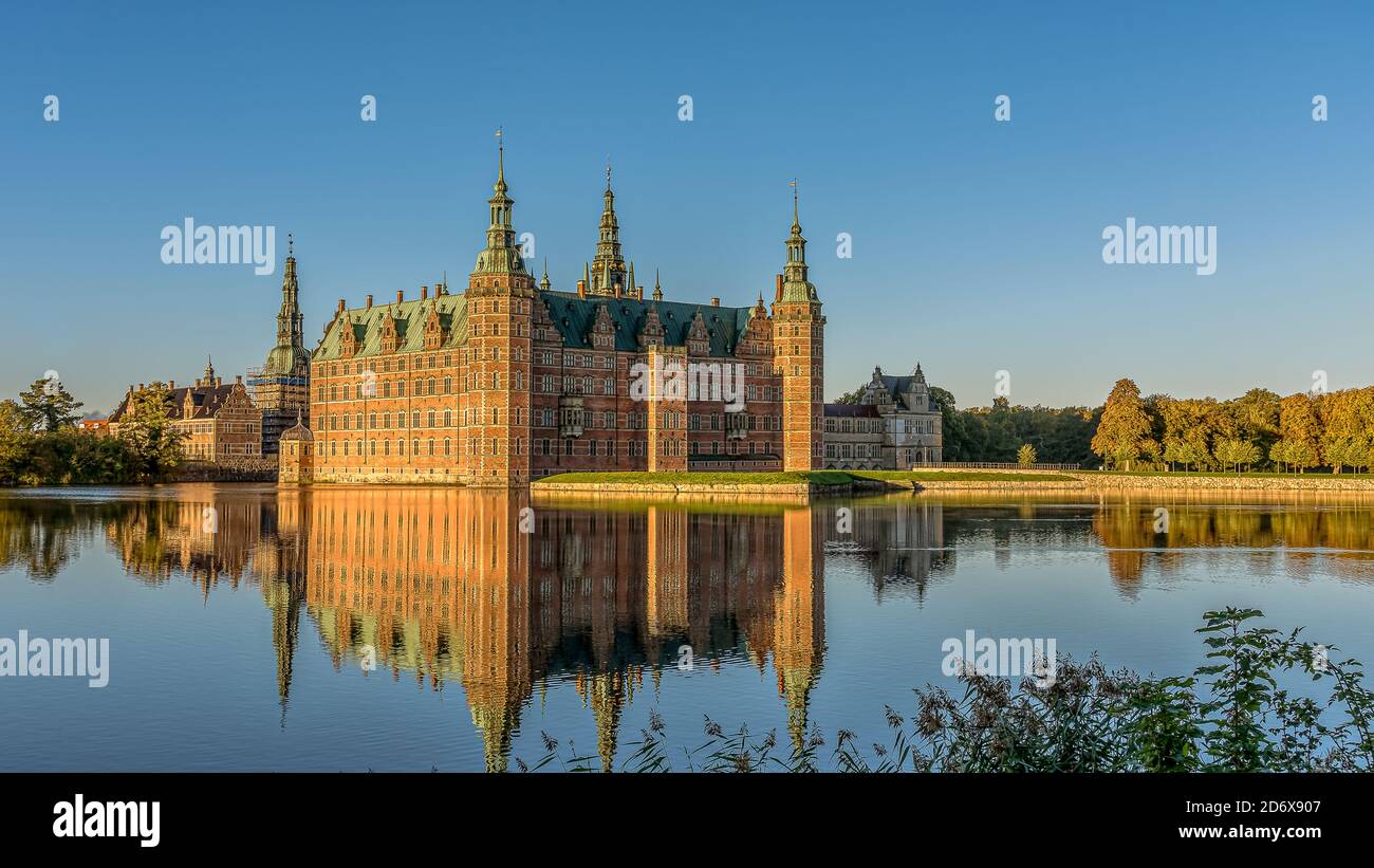 Frederiksborg Castello in un riflesso specchio-lucido nel lago appena dopo l'alba e alcune canne in primo piano, Hillerød, Danimarca, 17 ottobre 2020 Foto Stock