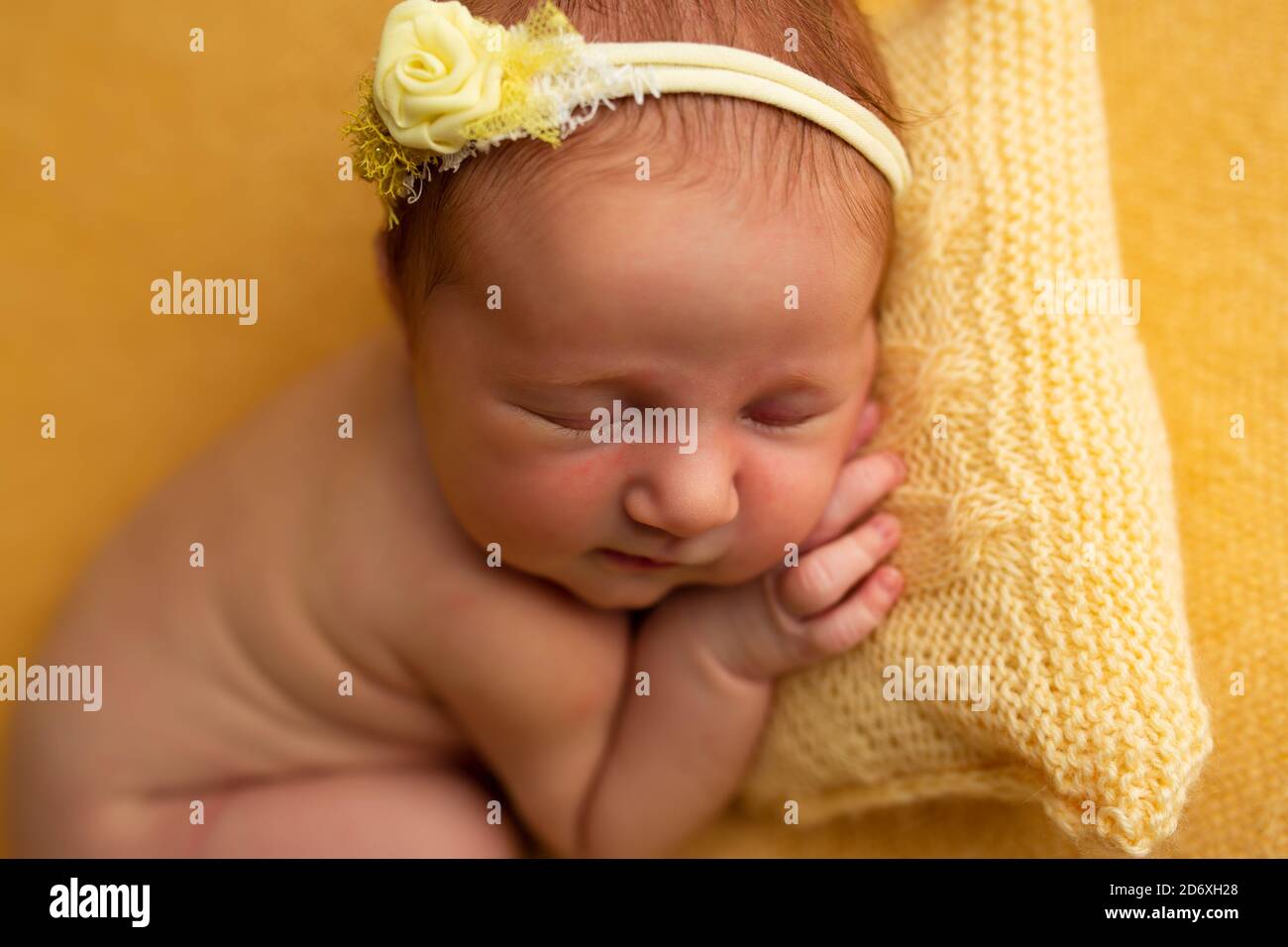 Simpatico bambino neonato che pappa sul cuscino su una coperta gialla Foto Stock