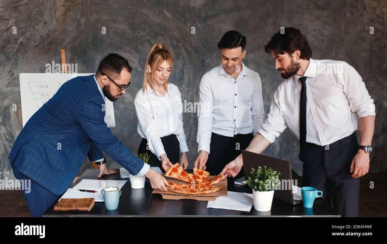 Felici i diversi colleghi trascorrono il lavoro pausa insieme mangiare take away consegna pizza in ufficio, sorridendo dipendenti multirazziali divertirsi, ridere e chattare Foto Stock