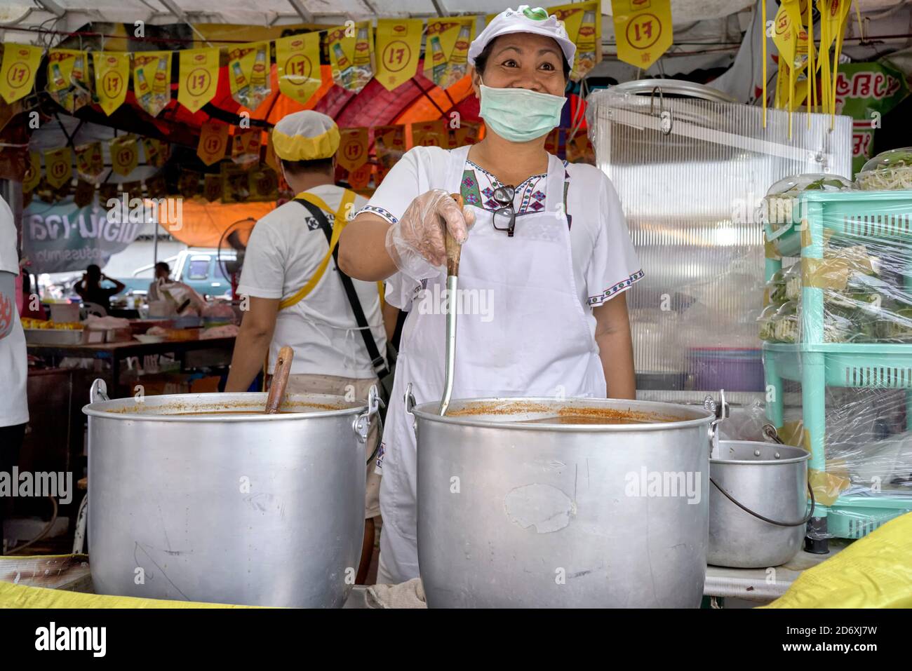 Nuovo normale. Rinomato Thailandia sorriso nascosto dietro una maschera viso. Una donna tailandese felice e sorridente fornitore di cibo alla sua bancarella di mercato. Thailandia, S. E. Asia. Foto Stock