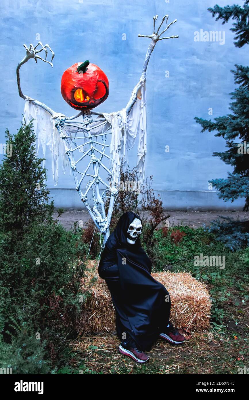 Un bambino in costume da morte si siede su una balla di fieno sotto un gigantesco scheletro di Jack Lantern ad un Halloween Garden Party. Festa del costume di tutti i Santi. Trucco Foto Stock