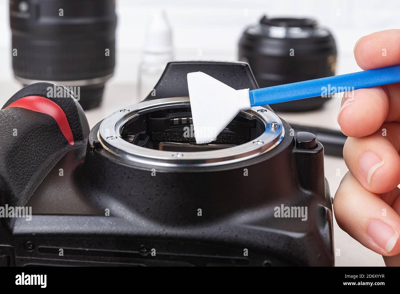 Tenendo con la mano un bastoncino bagnato sulla baionetta della fotocamera con l'obiettivo rimosso. Pulizia di routine di polvere e macchie da apparecchiature fotografiche. Primo piano di manutenzione. Foto Stock