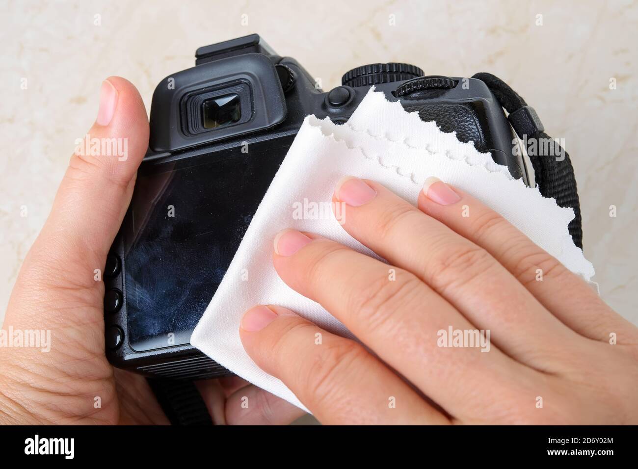 Le mani si intrecciano con un panno in microfibra sullo schermo della fotocamera dslr. Rimozione di routine di polvere e macchie di impronte digitali dalle apparecchiature fotografiche. Primo piano di manutenzione Foto Stock