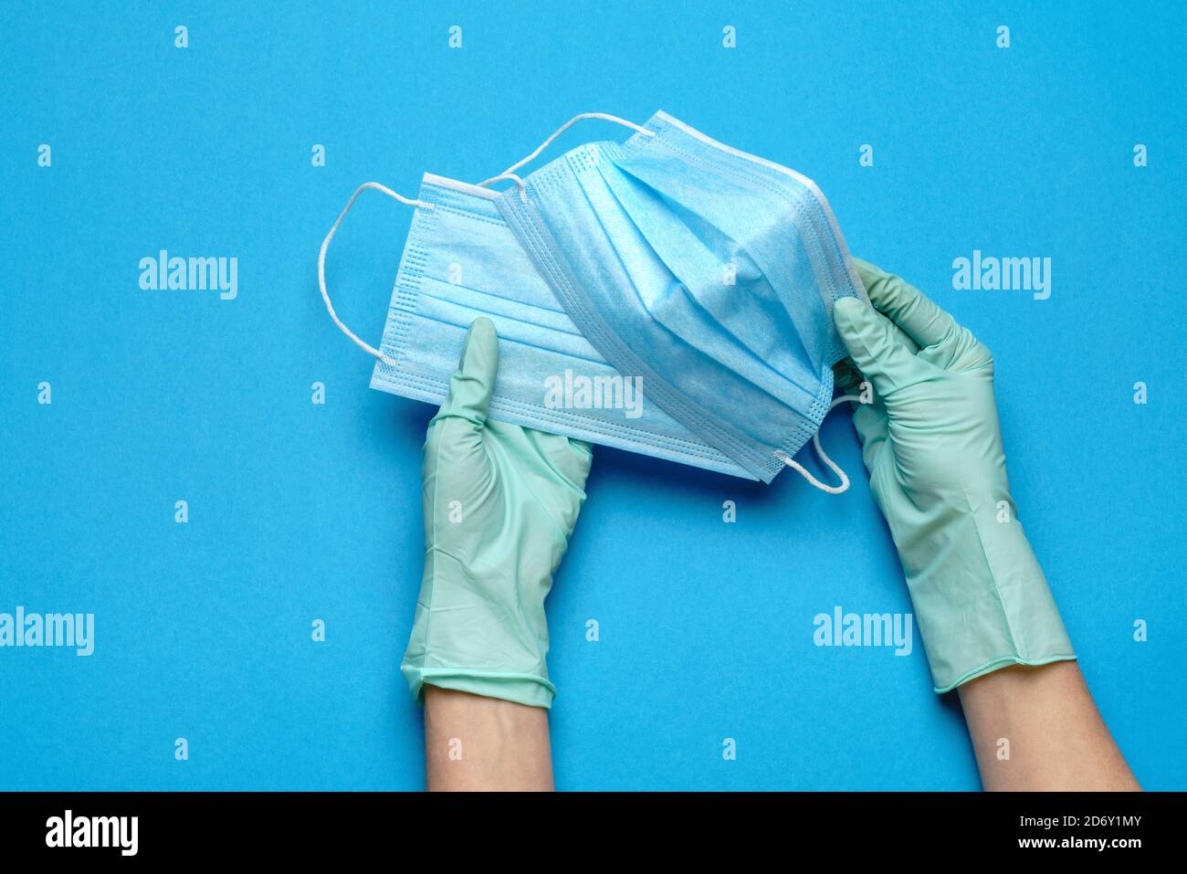 Mano umana in guanti protettivi che tengono isolata la maschera protettiva per il viso su sfondo blu Foto Stock