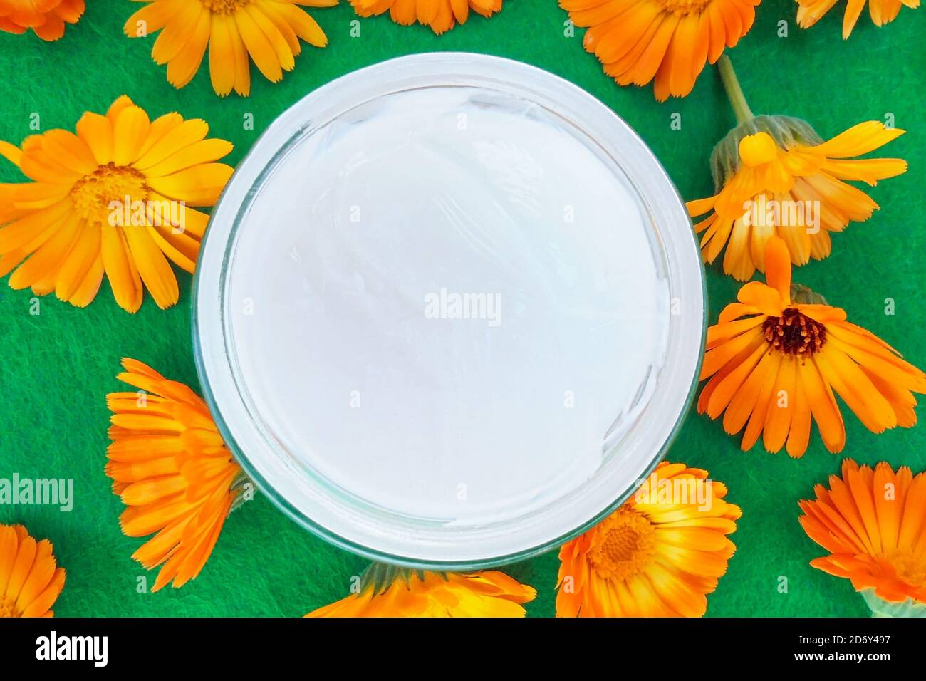 vasetto rotondo in vetro aperto con crema bianca e fiori di color arancio su fondo testurizzato verde. vista dall'alto Foto Stock