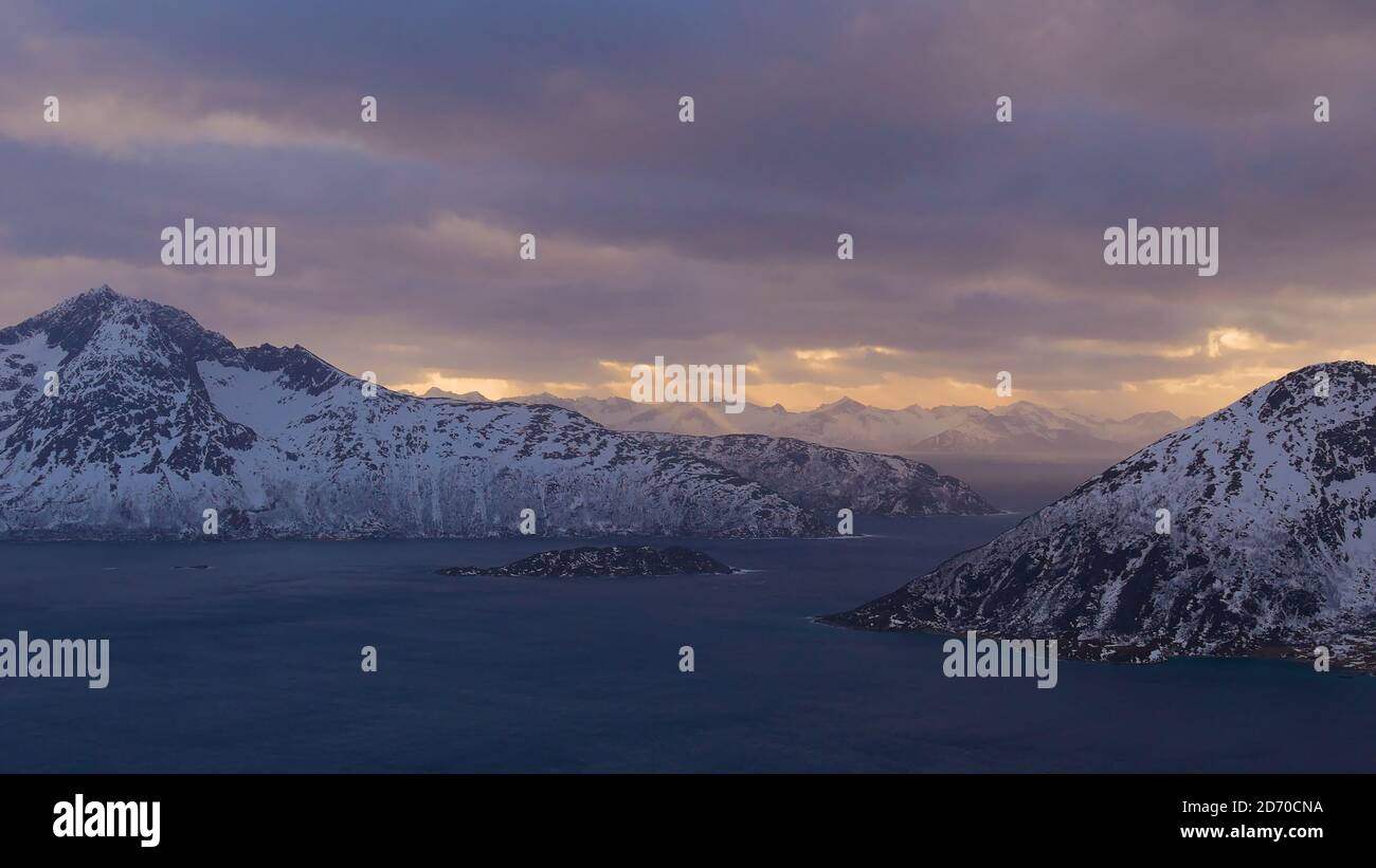 Maestoso panorama del sole del pomeriggio che splende attraverso le nuvole con raggi solari visibili sui fiordi (Sessøyfjord) vicino a Rekvik, Troms og Finnmark, Norvegia. Foto Stock