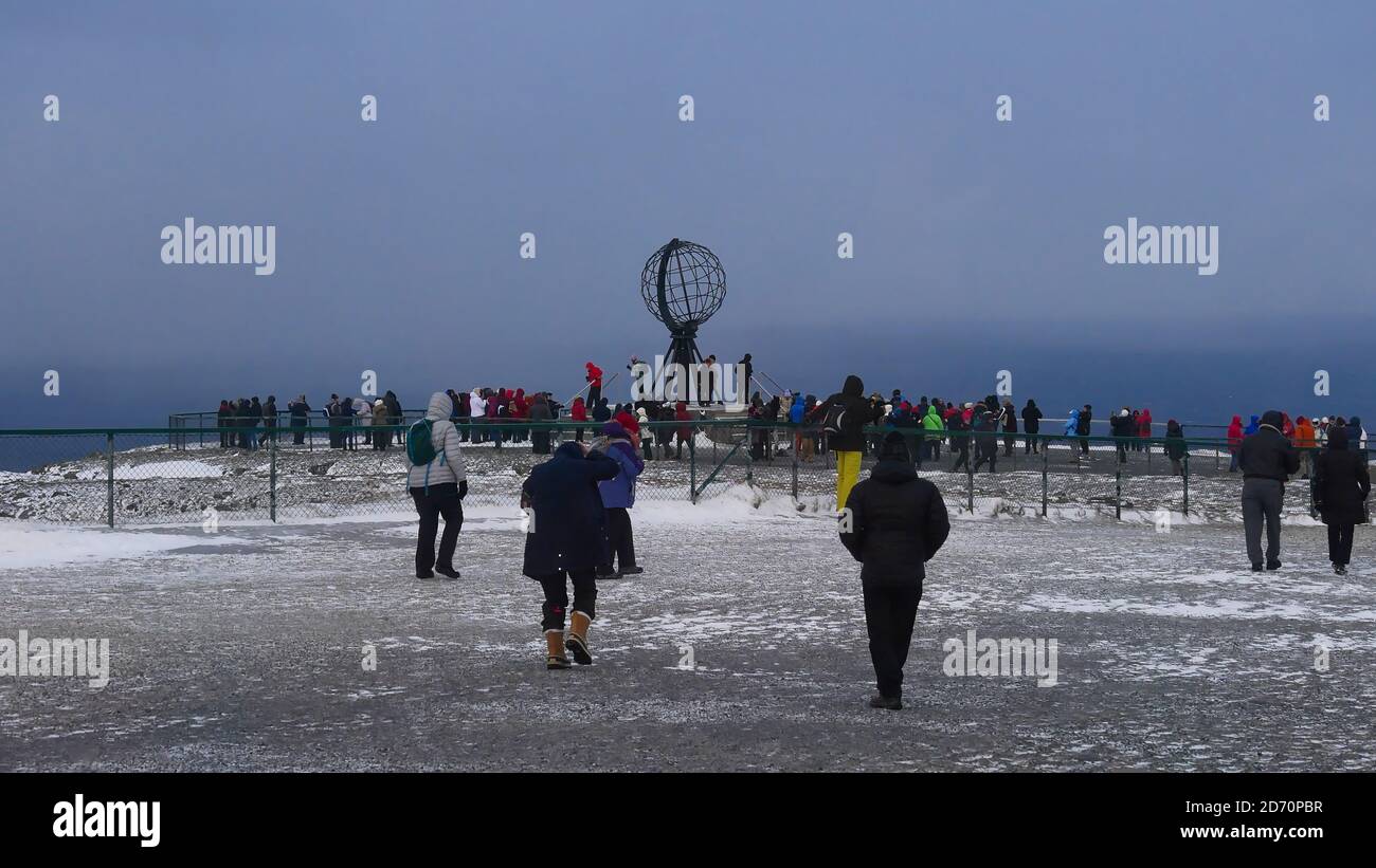 Nordkapp, Norvegia - 02/28/2019: I turisti da una nave da crociera Hurtigruten in un tour di un giorno a Capo Nord che si riuniscono intorno alla scultura popolare del globo in inverno. Foto Stock