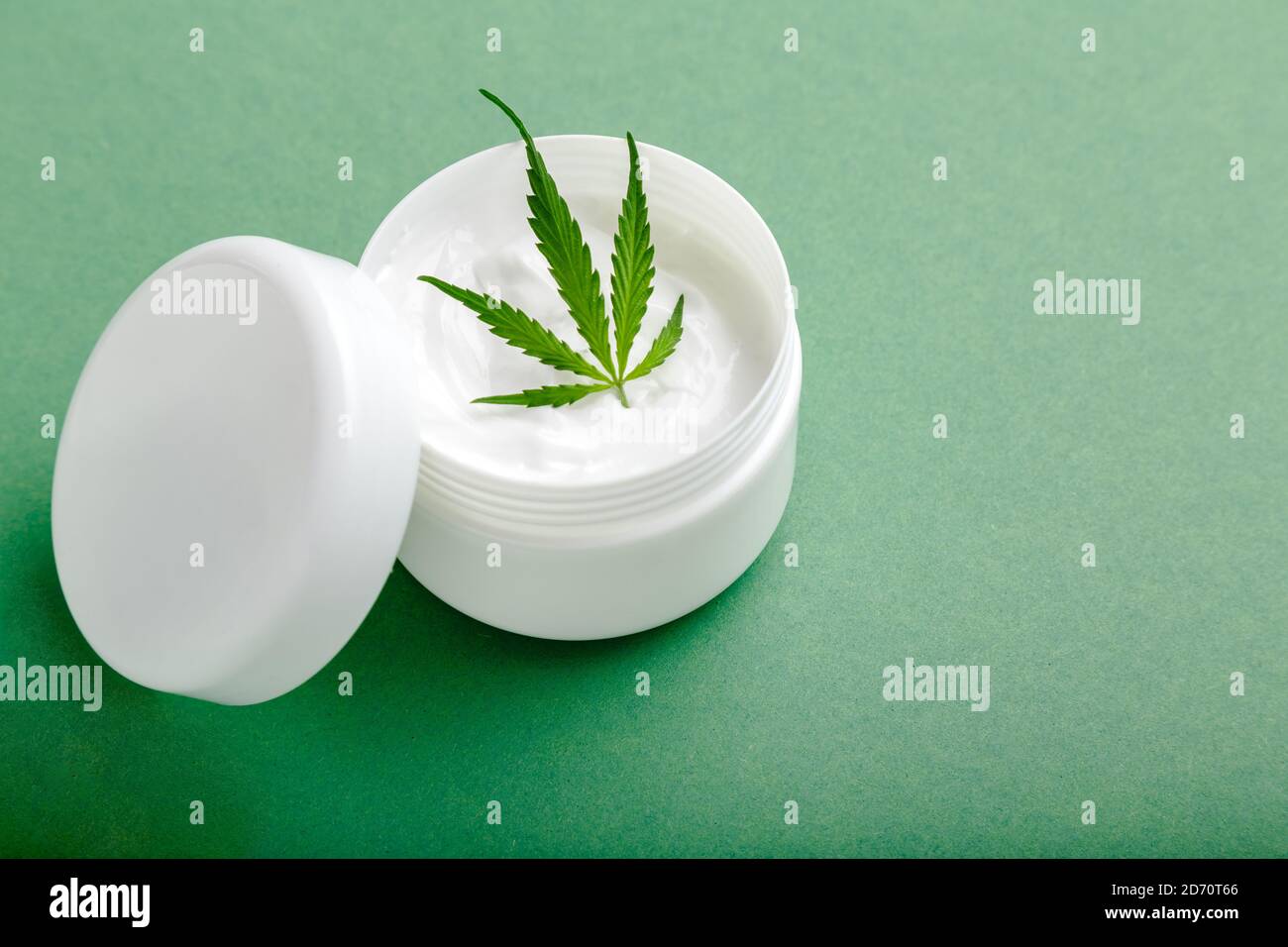 Crema idratante in vaso bianco con foglia di cannabis a base di olio CBD su sfondo verde con spazio per la copia Foto Stock