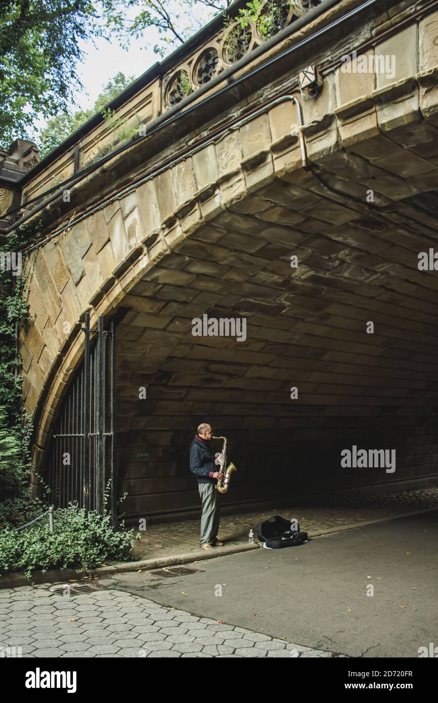 MANHATTAN, STATI UNITI - Set 24, 2020: Un uomo che gioca il sassofono sotto un arco in luce debole in Central Park a New York Foto Stock