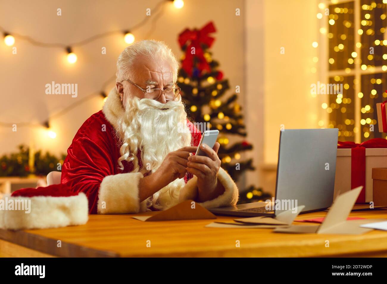 Santa moderna utilizzando il cellulare per leggere le e-mail dai bambini e. l'ordine presenta la consegna Foto Stock