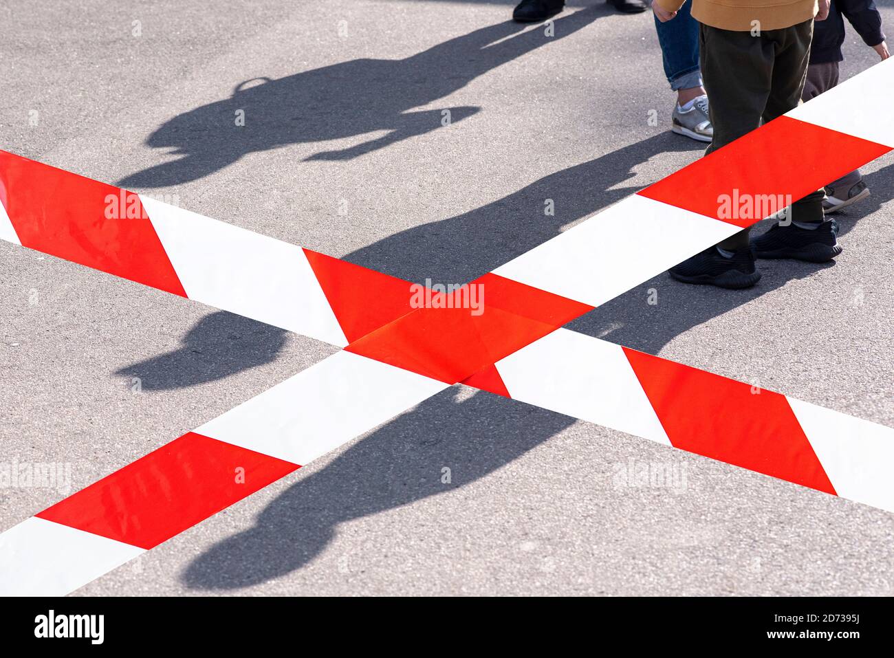 Linea rosso-bianca, nastro e ombre dei bambini al parco giochi, vietato camminare durante l'epidemia di coronavirus Foto Stock
