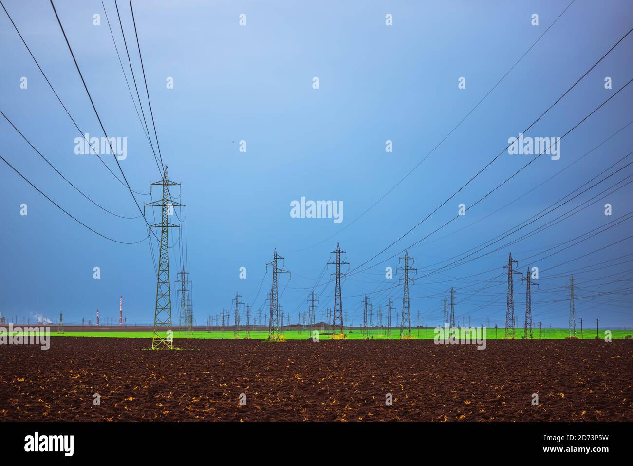 Campo agricolo, pali elettrici, torri di sottostazione, camini industriali e fabbrica Foto Stock