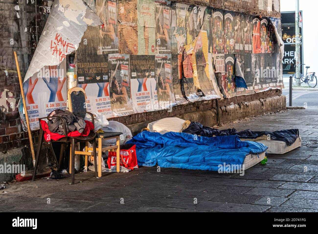 Casa di una persona senza casa con due materassi, sedie, biancheria da letto e scopa sotto un ponte ferroviario a Mitte, Berlino Foto Stock