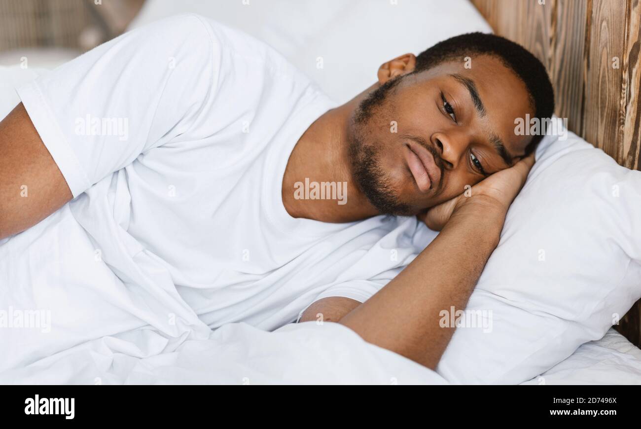 Depresso guy afro-americano sdraiato sveglio a letto a casa Foto Stock