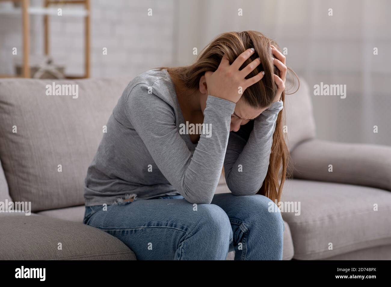 Infelice giovane donna con testa in mano seduta sul divano, piangendo e sentendosi depresso Foto Stock