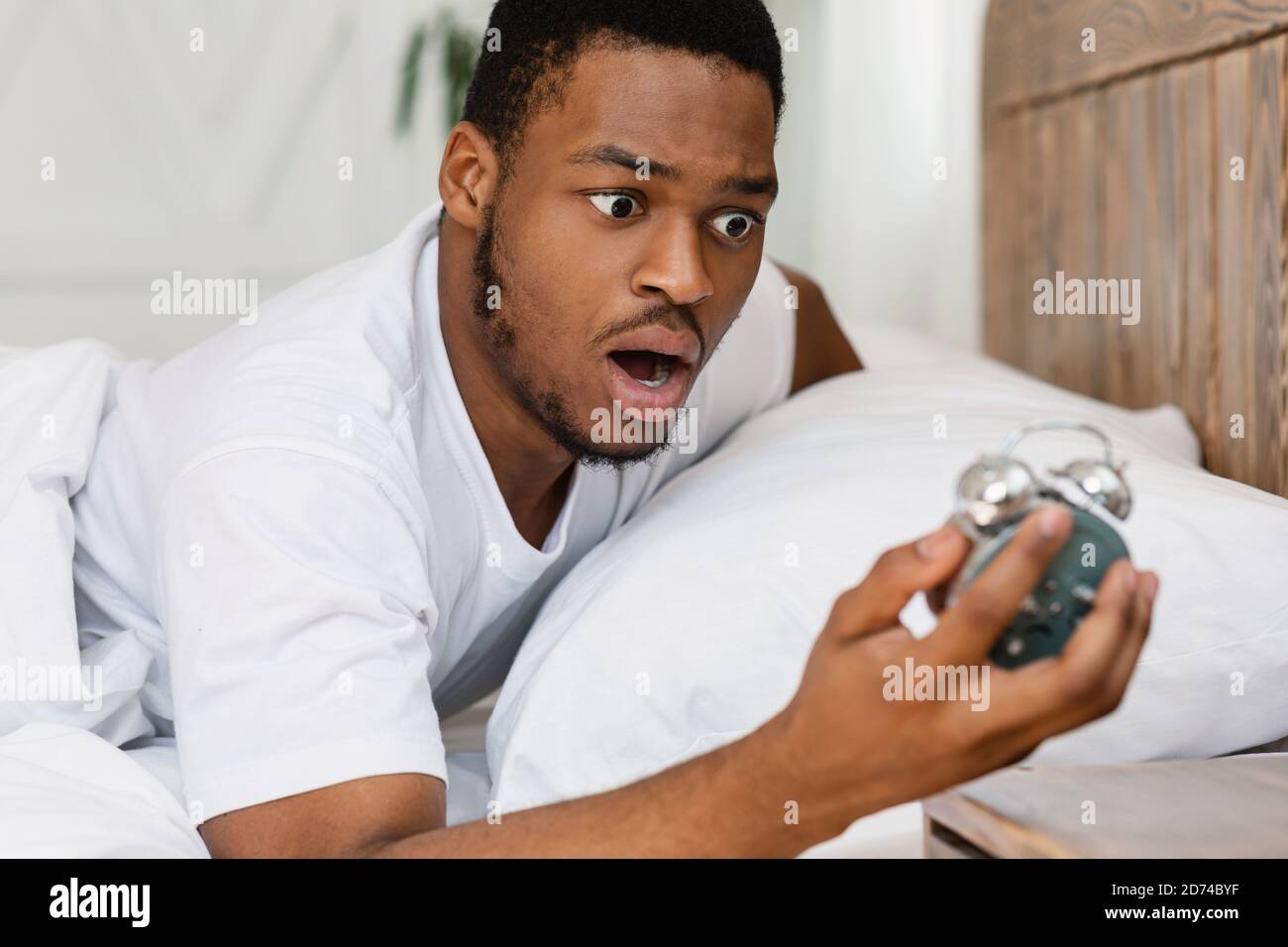 Scioccato Black Guy guardando sveglia svegliarsi oversleeping in interni Foto Stock