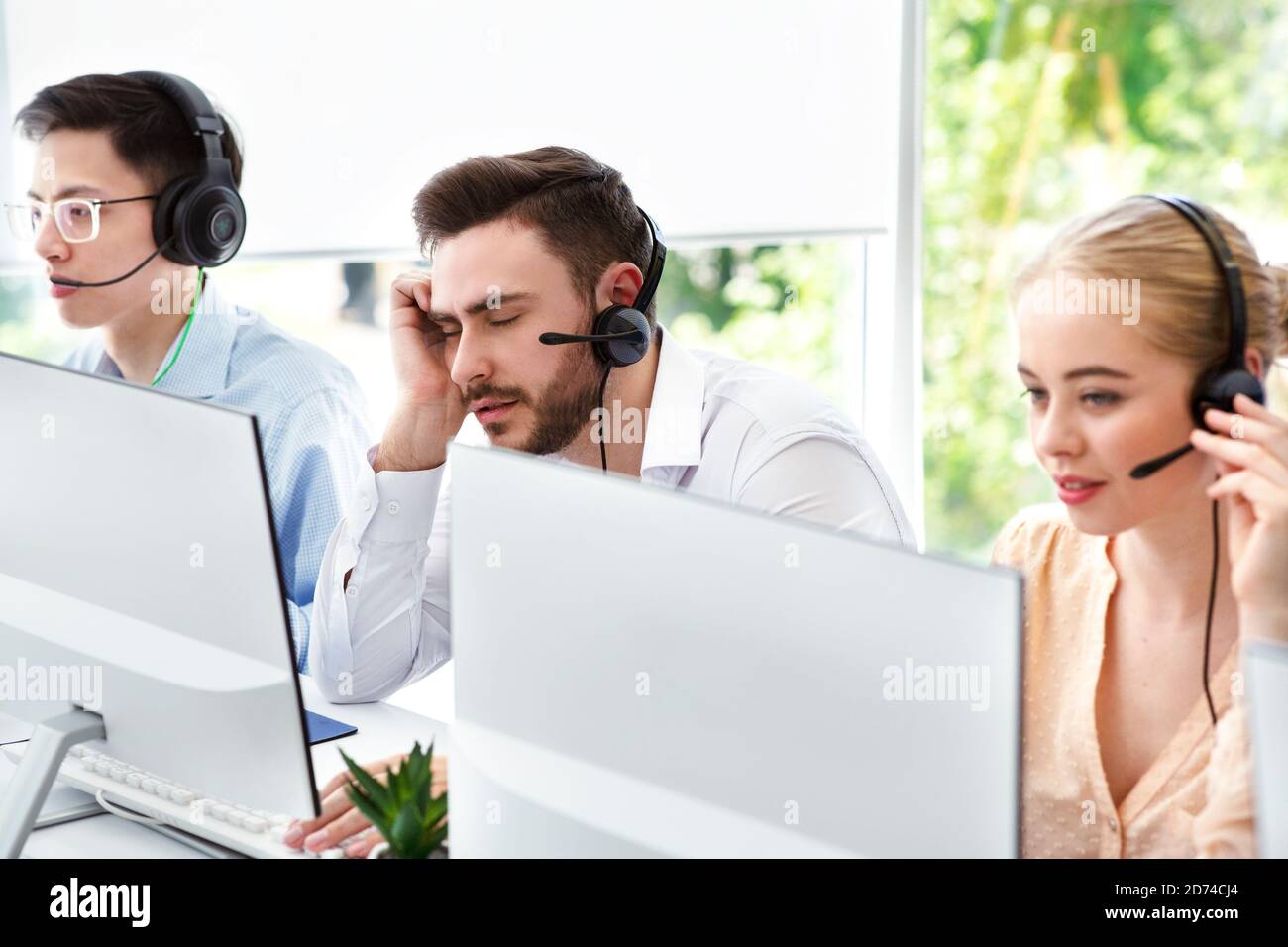 Un rappresentante del call center stanco e i suoi colleghi al lavoro ufficio open space Foto Stock