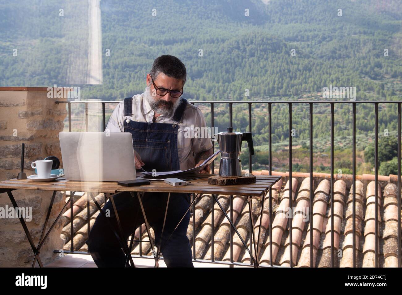 Uomo che lavora su un computer portatile sul balcone della sua casa con la natura. Foto Stock