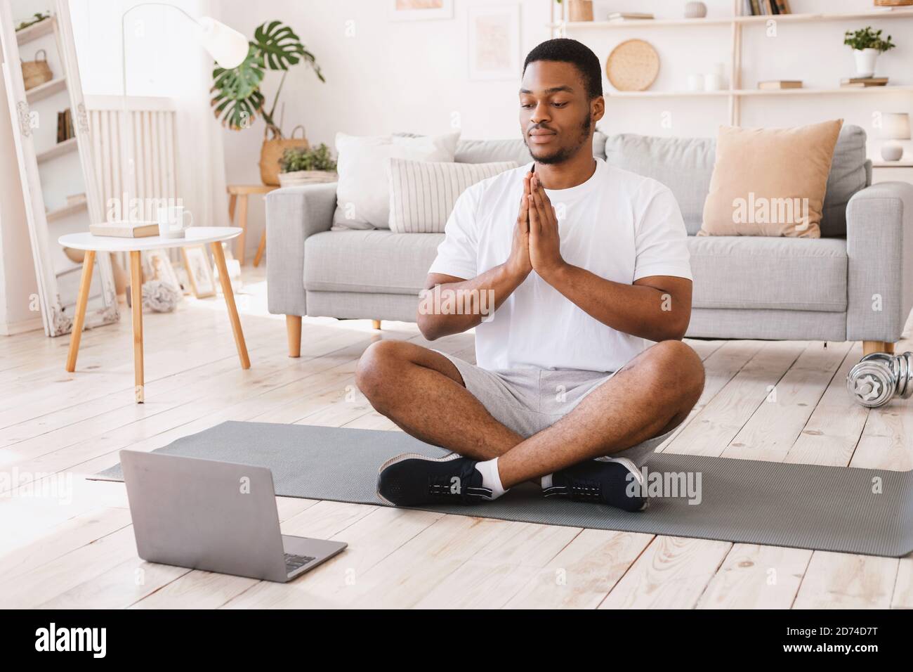 L'uomo afroamericano che fa lo yoga seduto al laptop a casa Foto Stock