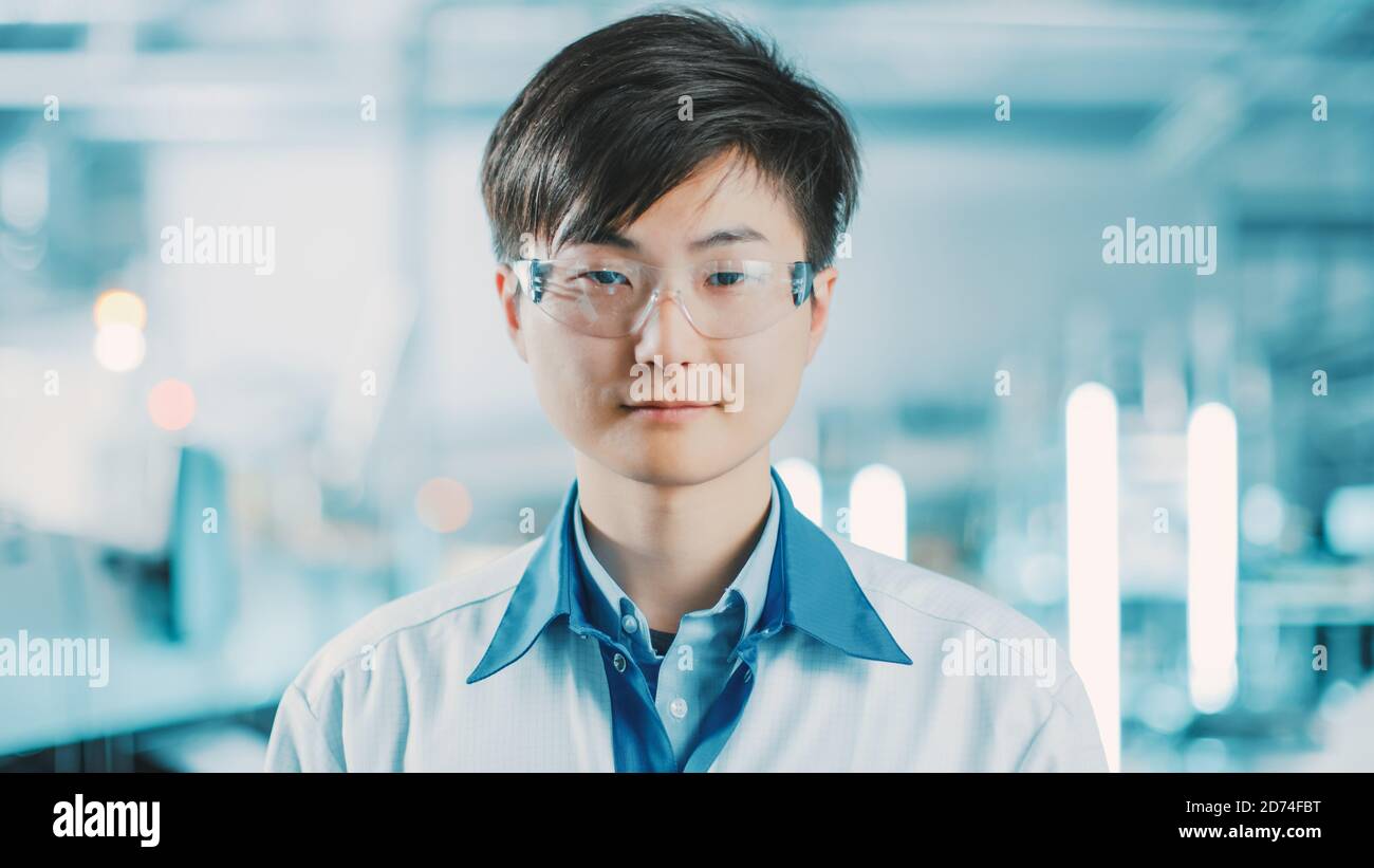 In High-Tech Factory: Ritratto del lavoratore asiatico indossare uniforme e occhiali di sicurezza. In background linea di assemblaggio elettronica sfocata con brillante Foto Stock