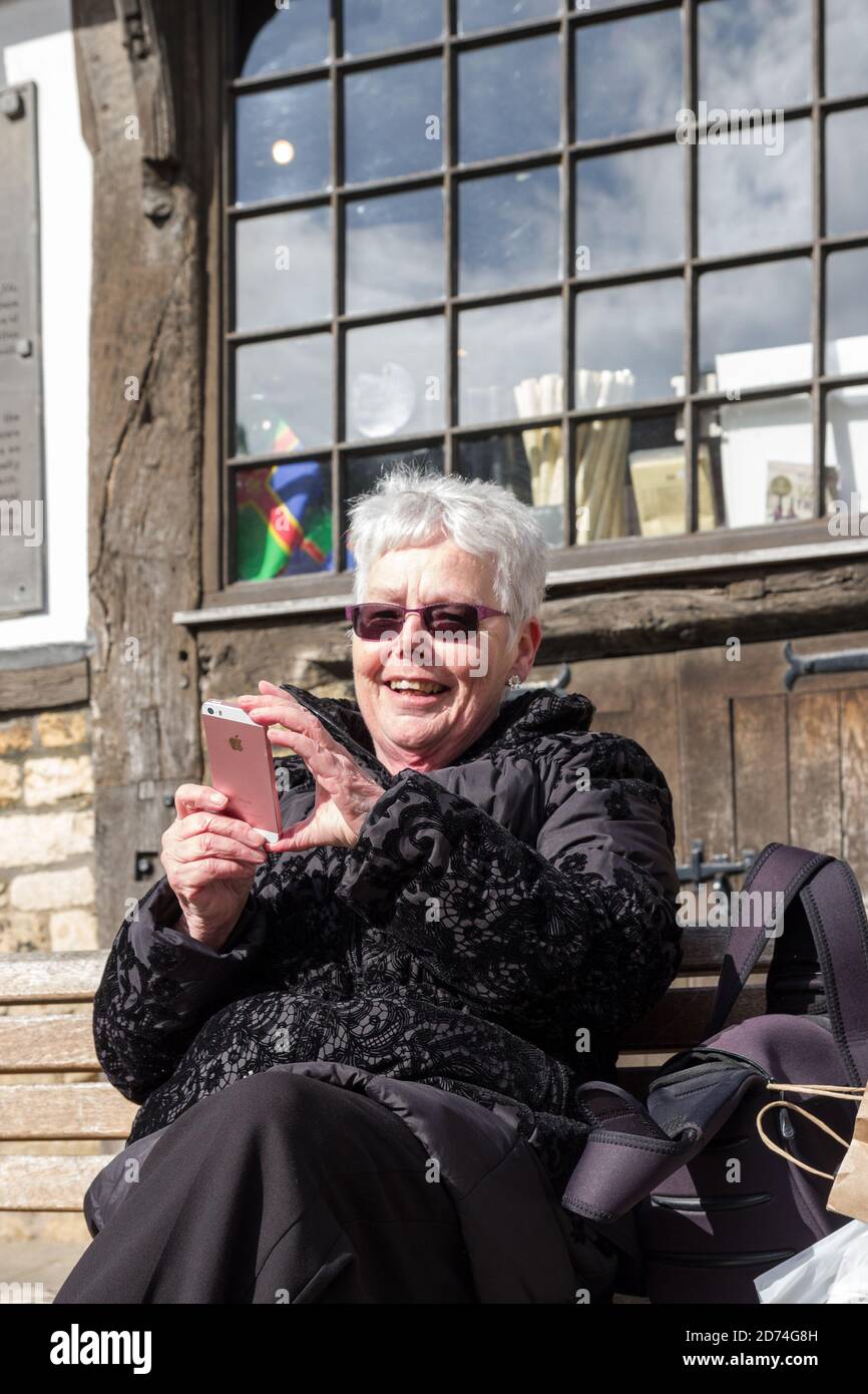 Donna anziana sorridente che controlla il telefono cellulare all'aperto, Regno Unito Foto Stock