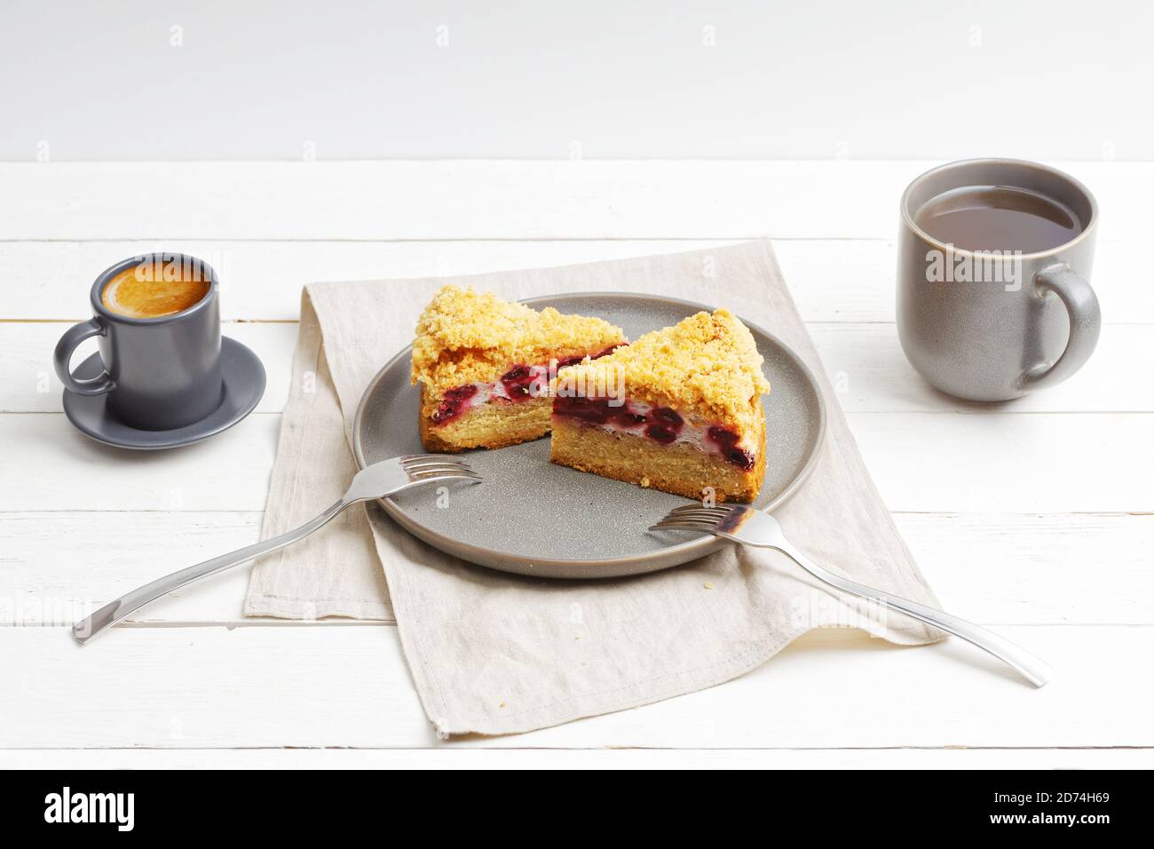 Due pezzi di torta di ciliegia fatta in casa con briciole sulla parte superiore e due tazze con caffè e tè su tavolo di legno bianco. Foto Stock