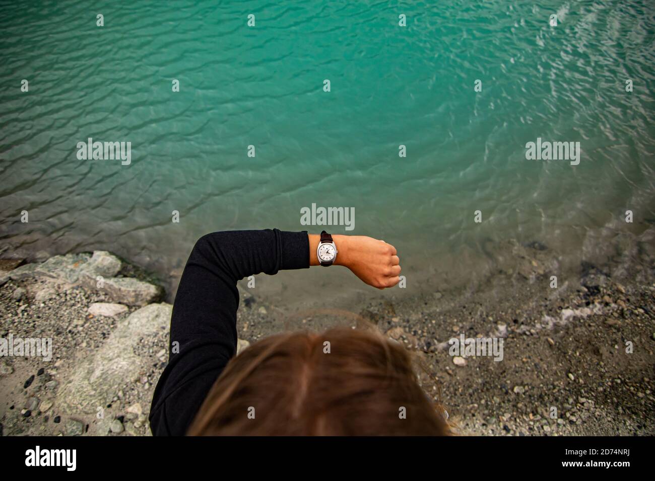 Donna sportiva che controlla orologio mentre si esercita all'aperto vicino al lago blu Foto Stock