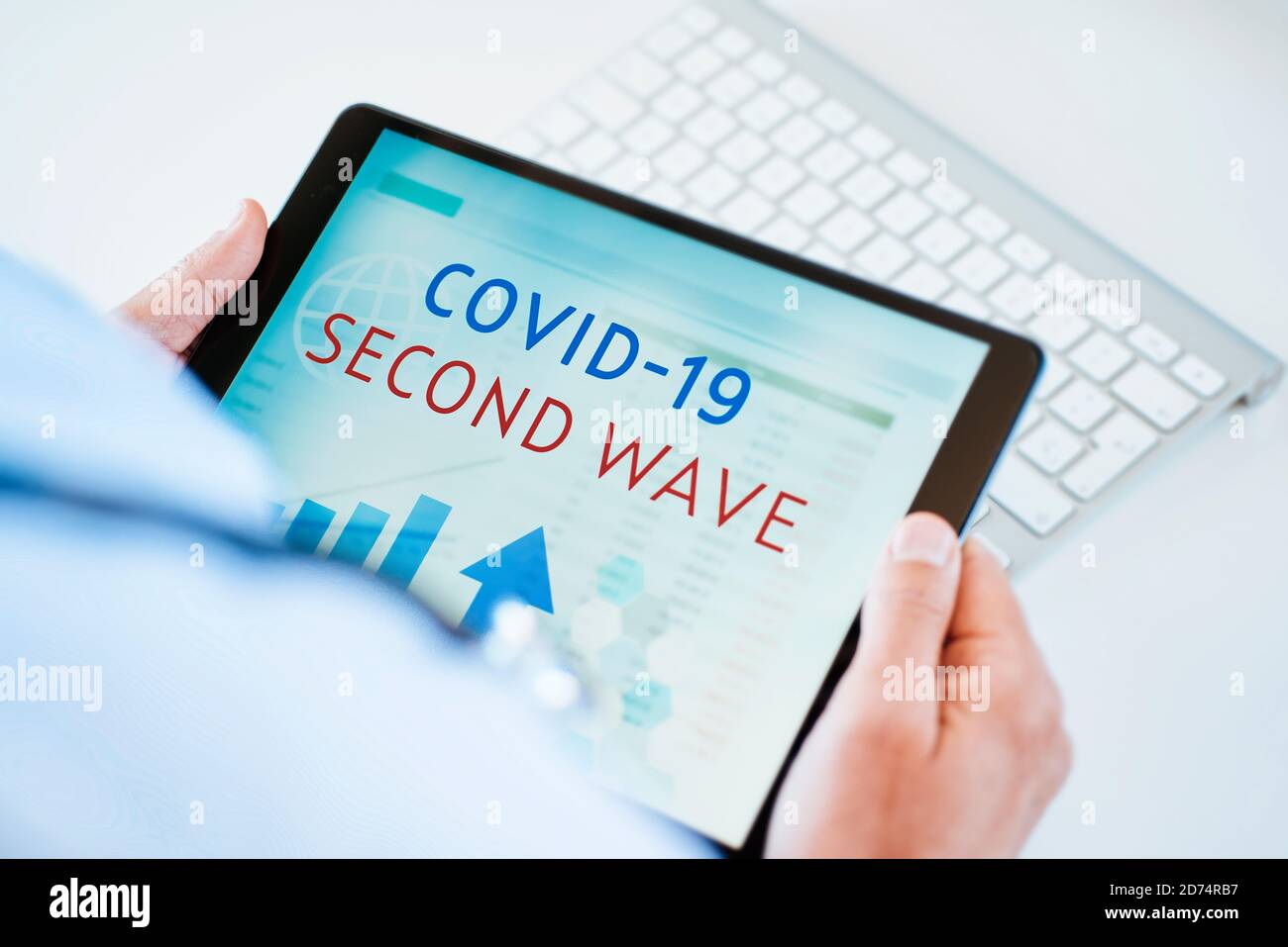 primo piano di un medico, seduto alla sua scrivania, con un tablet digitale in mano con il testo covid-19 seconda onda nel suo schermo Foto Stock