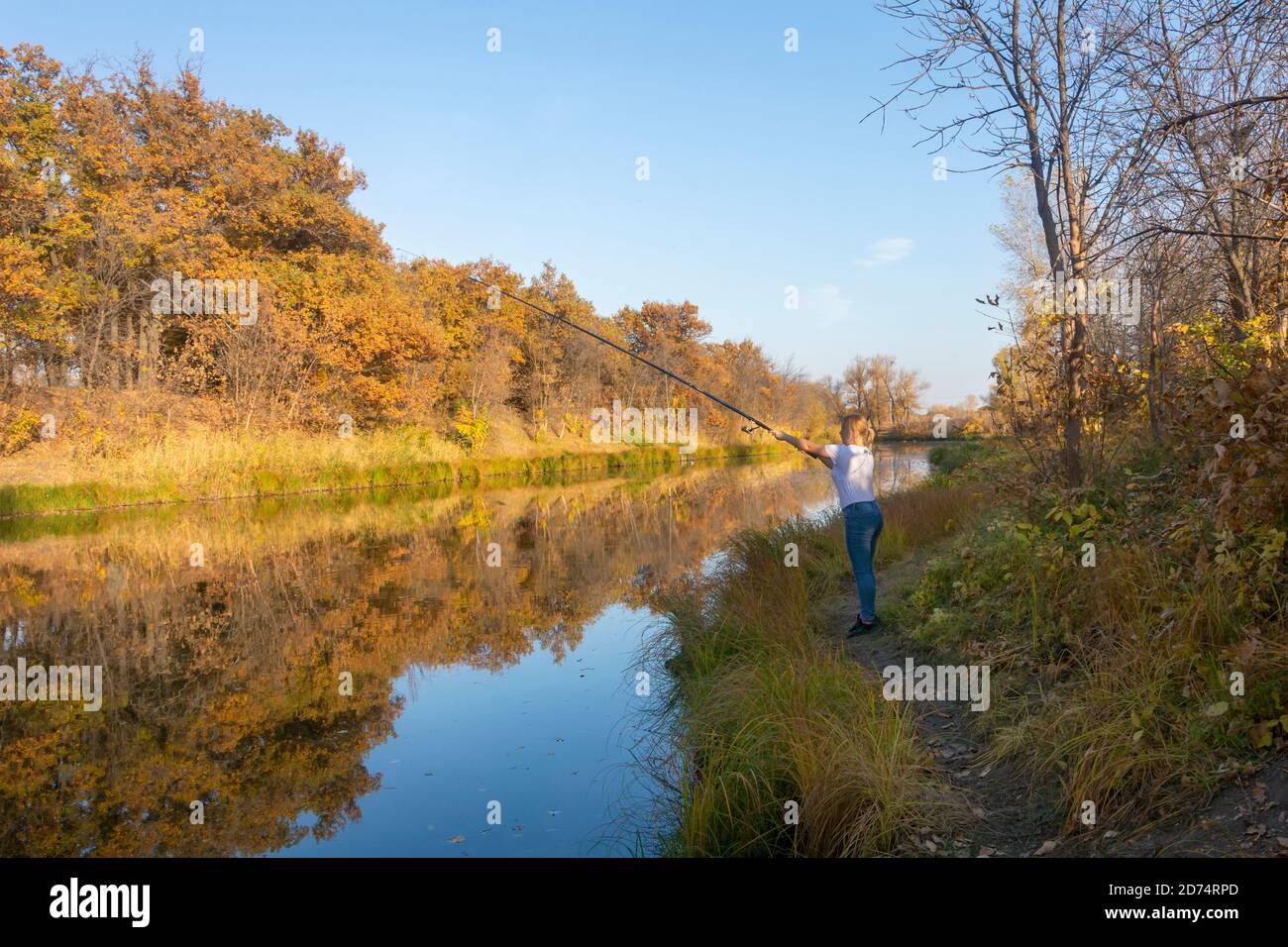 Giovane pescatrice cattura pesce con canna da pesca in autunno sul fiume. Concetto di giorno del pescatore. Foto Stock