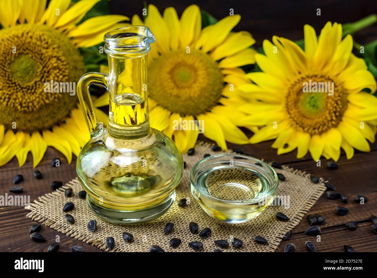 Olio di girasole in bottiglia e semi di girasole vicino a fiori di girasole freschi su sfondo di legno. Foto Stock