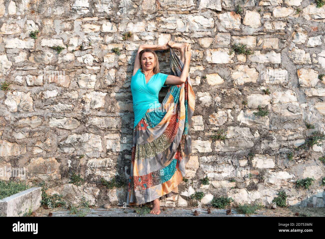 Donna adulta fa esercizio sportivo. Insegnante di yoga che fa un asana sulle mura della città vecchia. Foto Stock