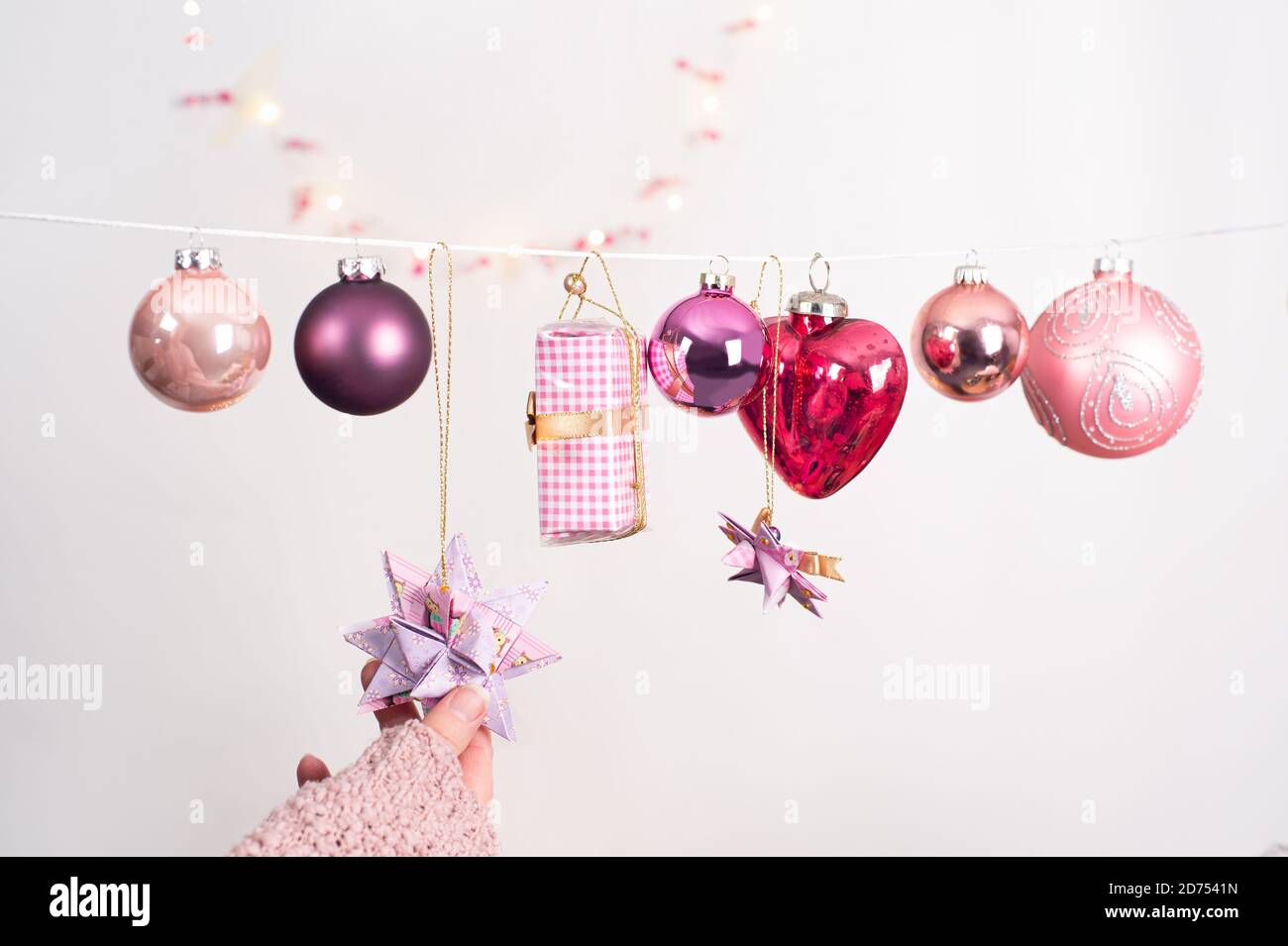 Immagine di Natale con diverse palle in colori di bacche. Piccolo regalo e tree pendenti appesi su una corda. La mano di una donna tocca un Fröbelster Foto Stock