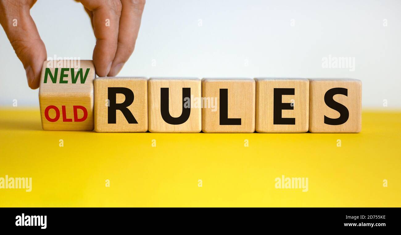 La mano maschile trasforma un cubo e cambia le parole 'vecchie regole' in 'nuove regole' su un bel tavolo giallo, sfondo bianco. Business e covid-19 conc pandemico Foto Stock