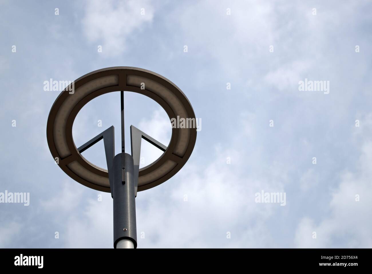 Una lampada rotonda grigia con base a LED nera tre supporti ramificati montati su un palo cilindrico contro un cielo blu coperto di nuvole bianche Foto Stock