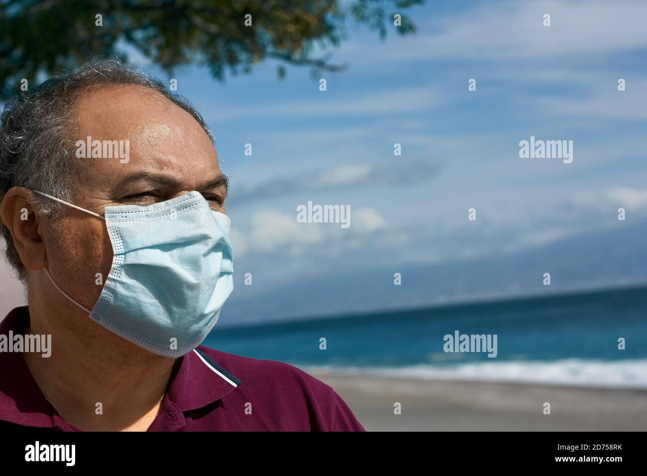 L'uomo indossa una maschera chirurgica, si erge sul lungomare e guarda in lontananza. Rispettare la distanza sociale in tempi di pandemie, covid-19. Foto Stock