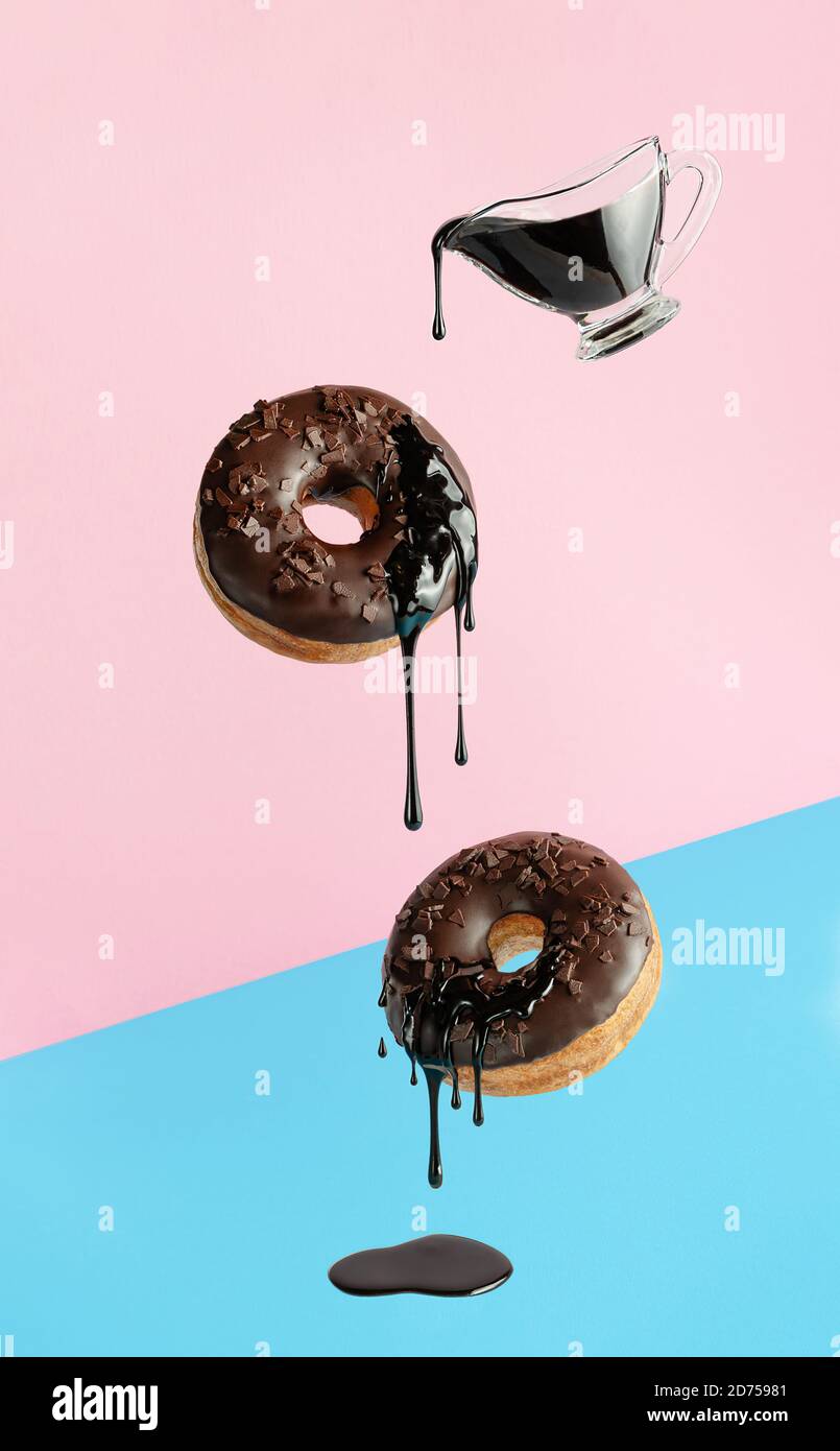 Ciambelle volanti con cioccolato gocciolante su sfondo blu rosa. Design pop art Foto Stock