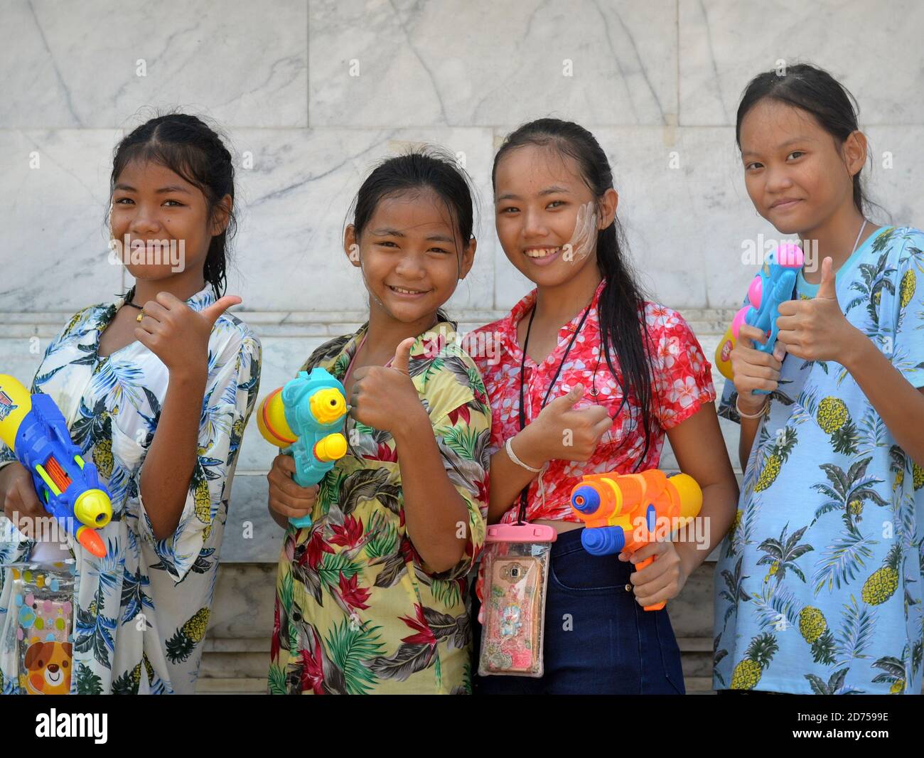 Quattro ragazze pre-teen di Bangkok trasportano le pistole dell'acqua di plastica, danno i pollici-in su il gesto e il sorriso per la macchina fotografica durante il festival dell'acqua di primavera di Songkran. Foto Stock