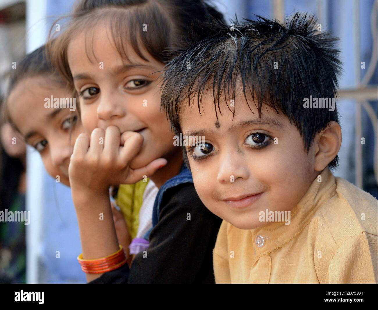 Tre piccoli bambini indiani Rajasthani con il tradizionale kohl eyeliner sedersi in una fila e posa per la macchina fotografica. Foto Stock