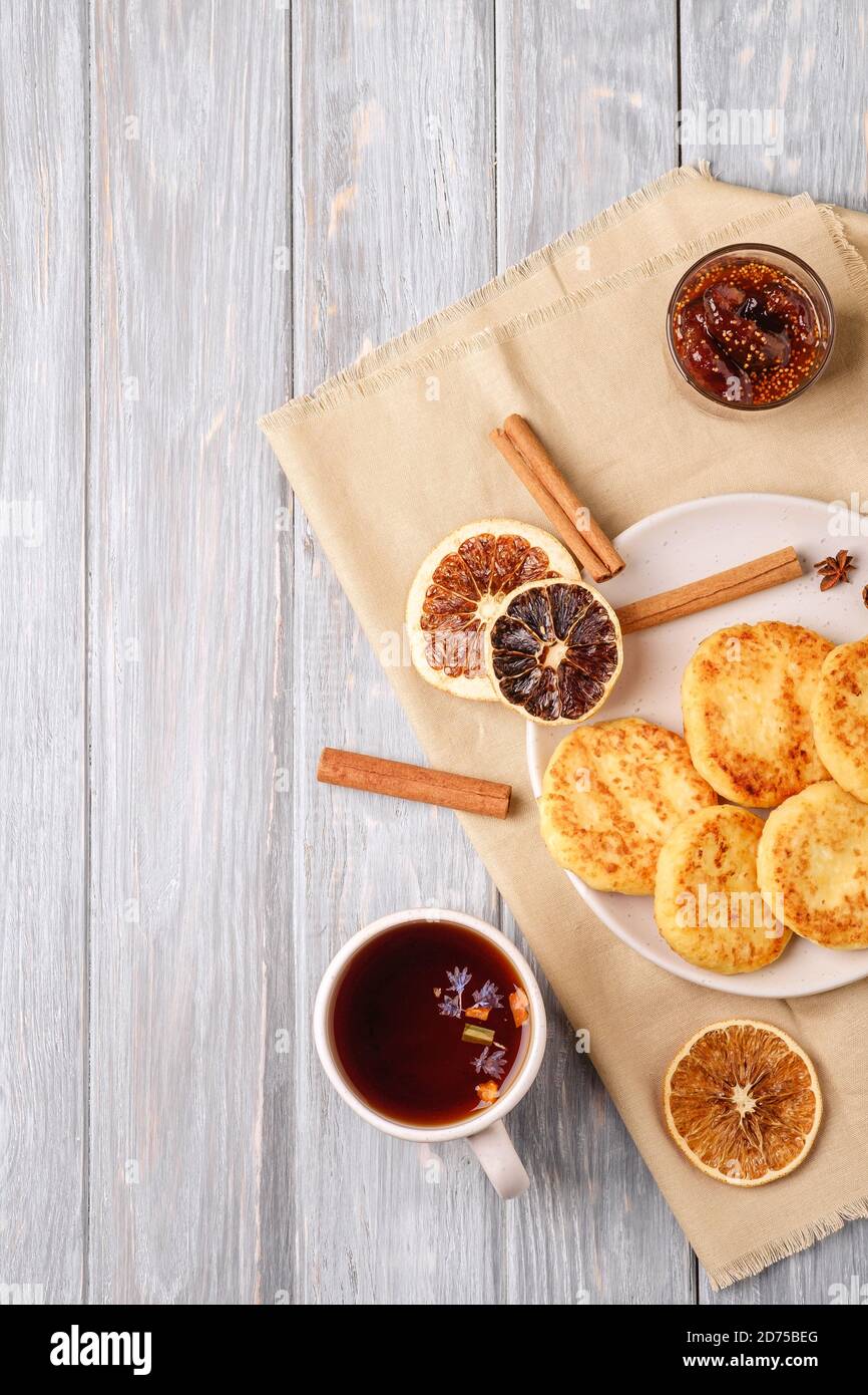 Frittelle di formaggio cottage con tè nero aromatico caldo, umore di prima colazione di Natale con anice, cannella e agrumi secchi su sfondo di legno, vista dall'alto Foto Stock