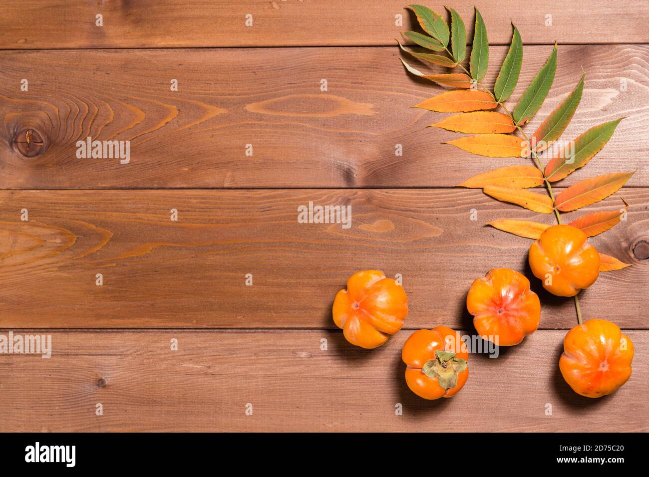 Abstract autunno ancora vita: Foglie giallite e persimmon maturo su un tavolo di legno. Disposizione piatta. Spazio di copia Foto Stock