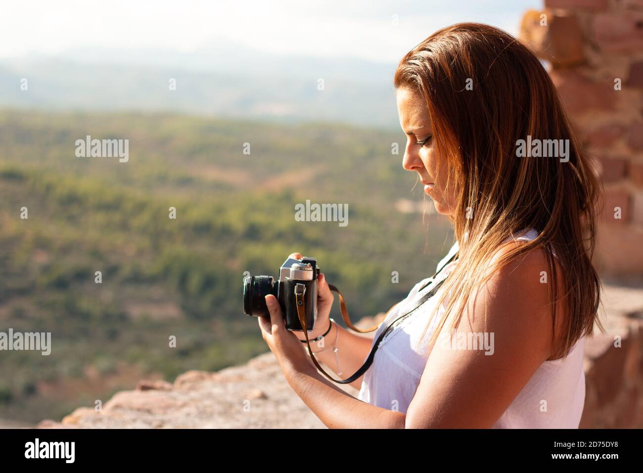 Una giovane donna ha una vecchia macchina fotografica imparando come usarla davanti ad un paesaggio. Concetto di fotografia Foto Stock